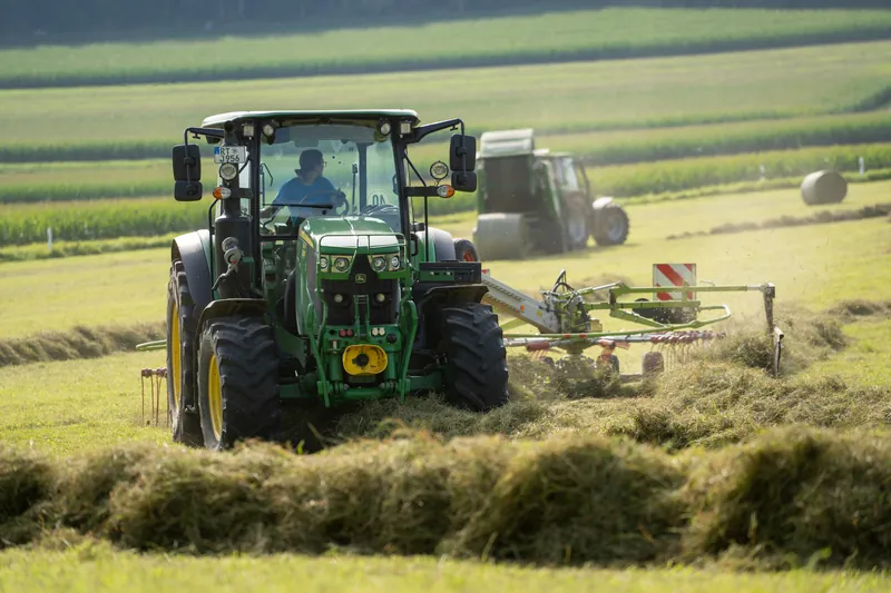 Grüner Traktor mit Schwader beim Heuwenden