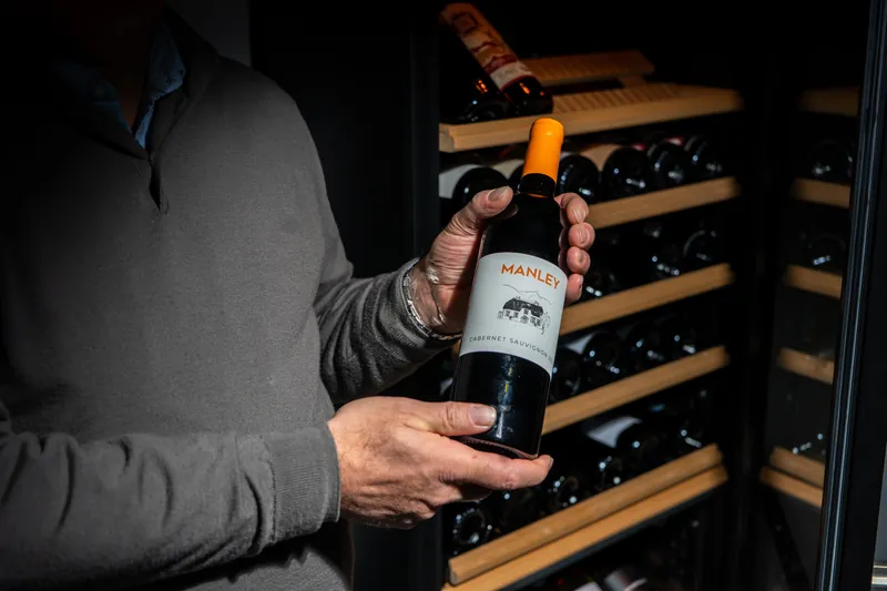 Hände präsentieren eine Flasche Rotwein vor dem Weinschrank